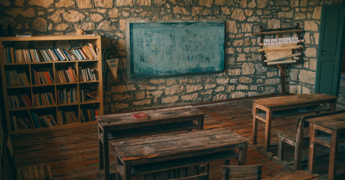An empty rustic classroom featuring stone walls, wooden desks, and a chalkboard, evoking a sense of nostalgia.